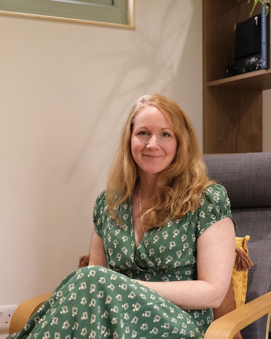 Charlotte, smiling, sitting in an armchair in her counselling room