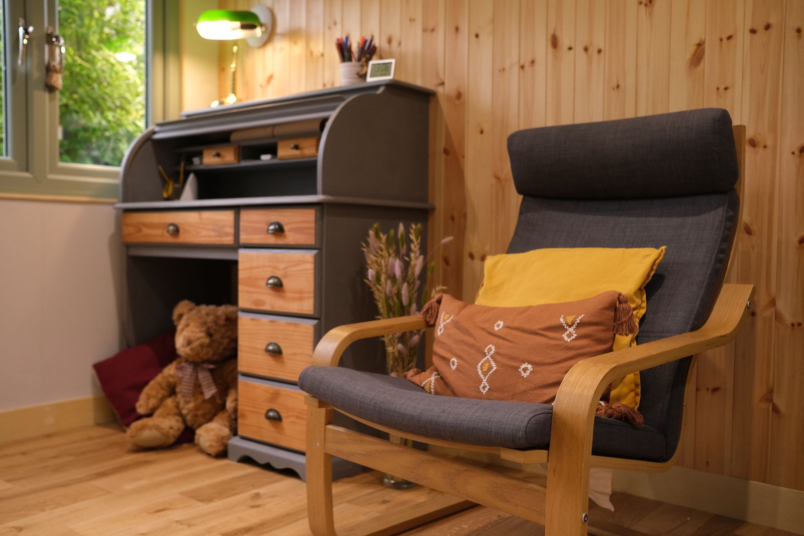 An armchair with mustard and terracotta cushions beside a wooden bureau in the counselling room