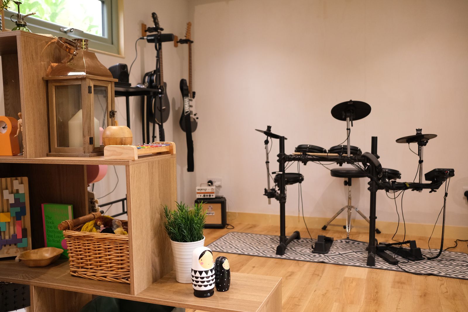 An electronic drum kit and guitars in the corner of the room, with shelves of games and baskets